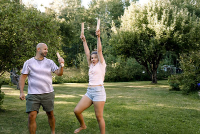 Father looking at daughter with hand raised while playing molkky in yard