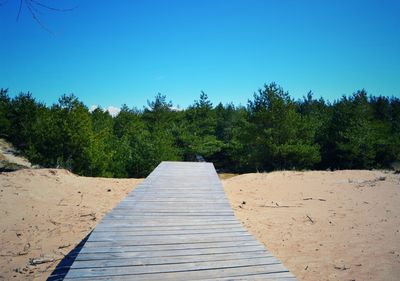Boardwalk amidst trees against clear blue sky