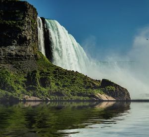 Scenic view of waterfall by lake against sky