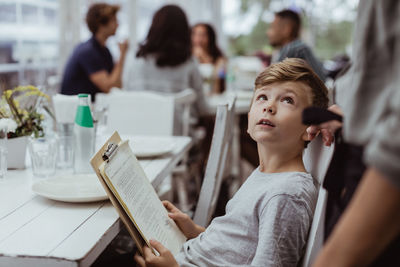 Boy holding menu card looking at woman while sitting in restaurant