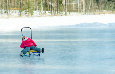 Full length of happy girl sitting on sled