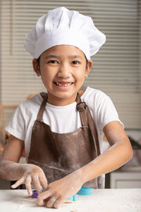 The little girl wore a white chef hat and a brown apron. the kid making cookies in the kitchen.