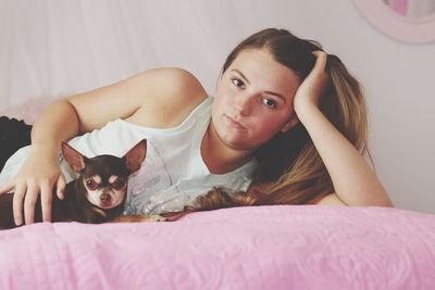 Portrait of young woman with chihuahua on bed at home