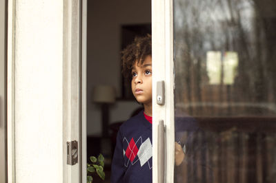 Thoughtful boy looking through window at home