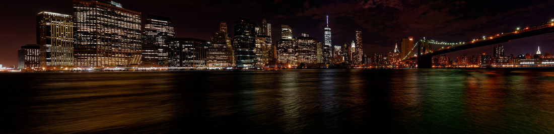 Illuminated bridge over river by buildings against sky at night