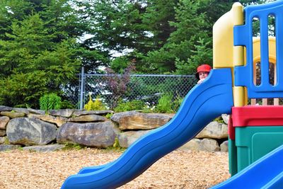 Side view of man sitting at playground against trees