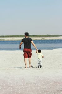Rear view of man with son walking on sand at beach against sky