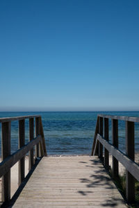 Wooden pier on sea against clear blue sky