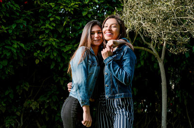 Portrait of smiling female friends standing against plants in park