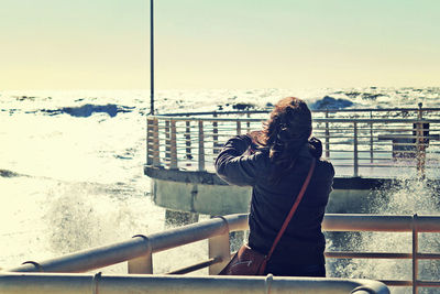 Rear view of woman standing on pier by sea against clear sky