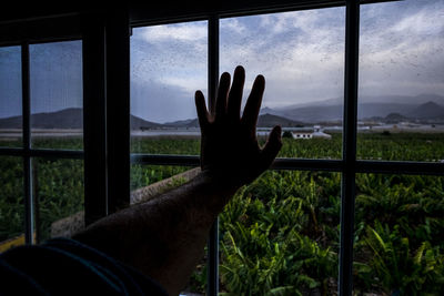 Human hand against sky seen through glass window