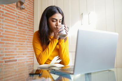 Young woman drinking coffee while sitting at office with laptop
