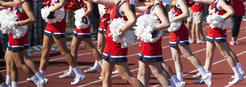 A group of high school cheerleaders during a high school football game using red and white pom poms.