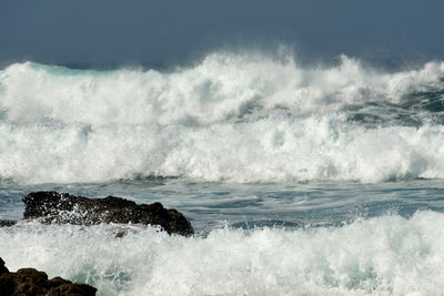 Waves splashing on shore against sky