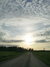 Road amidst field against sky during sunset