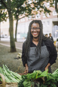 Portrait of happy female vendor with braided hair near stall at vegetable market