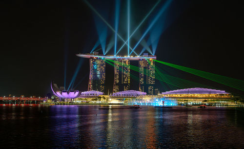 Illuminated marina bay sands by sea against sky