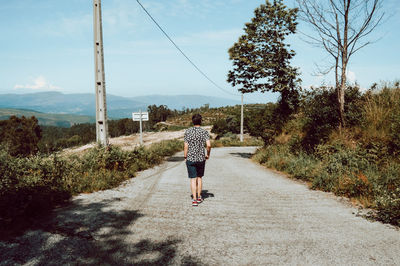 Rear view of man walking on road against sky