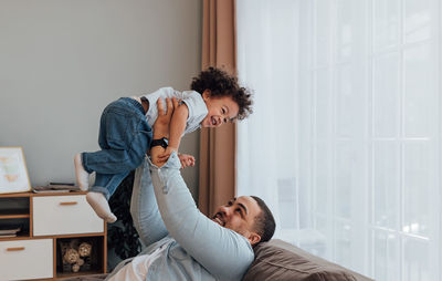 Father picking up son while relaxing on sofa at home