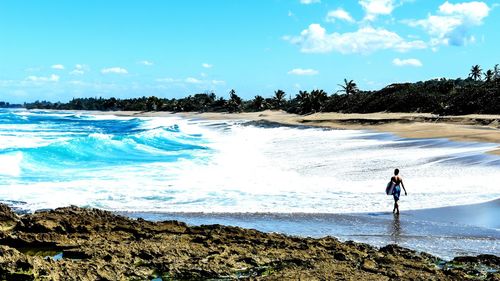 Rear view of man carrying surfboard on beach