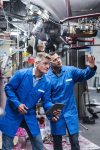 Male coworkers with digital tablet discussing while examining machinery in factory