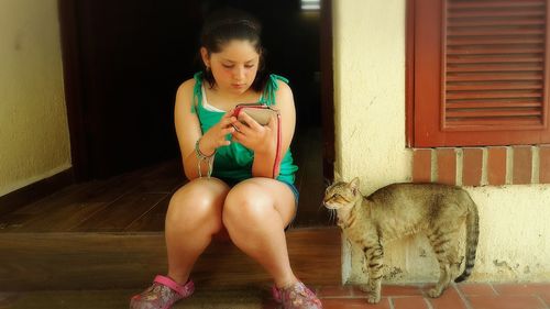 Girl using mobile by cat at porch