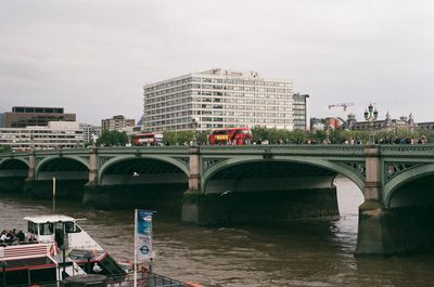 Bridge over river by buildings in city against sky