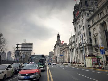 Cars on city street by buildings against sky