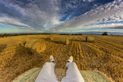Low section of man sitting on hay bale at field