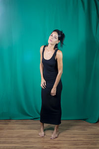 Portrait of standing adult model in black dress against dark green background. 