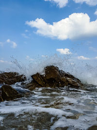 Sea waves splashing on rocks against sky