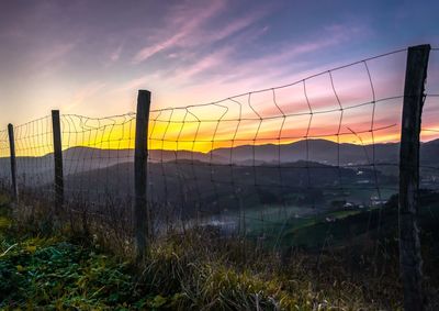 Fence on field against sky during sunset