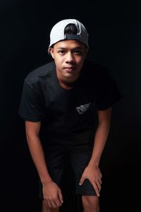 Portrait of young man standing against black background