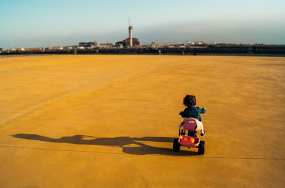 Rear view of girl riding tricycle on playground against sky