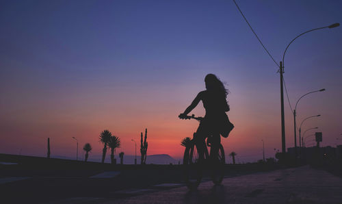 Silhouette woman jumping on street against sky during sunset