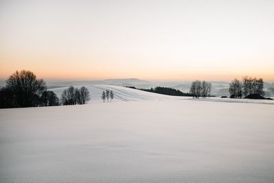 Snow covered field against sky during sunset