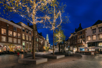 Illuminated street amidst buildings against sky at night