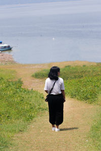 Rear view of woman walking on shore against sea