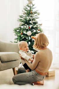 Brother and sister play together in a chair next to the christmas tree. kids have fun