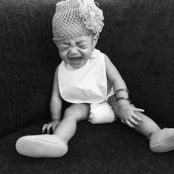 Cute baby girl crying while sitting on sofa at home