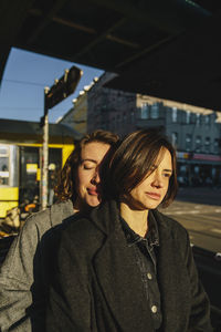 Affectionate young woman standing behind lesbian partner in city on sunny day