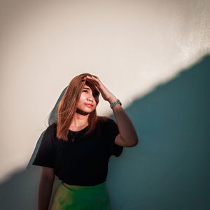 Young woman looking away while standing against wall