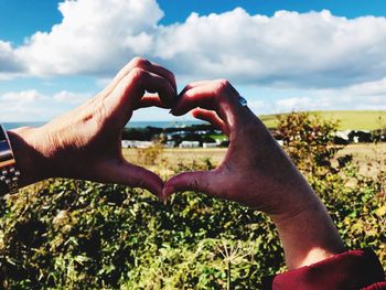 Midsection of man making heart shape against sky