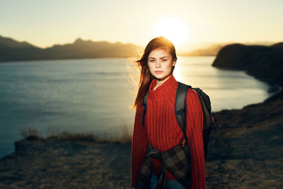 Portrait of young woman standing at beach during sunset