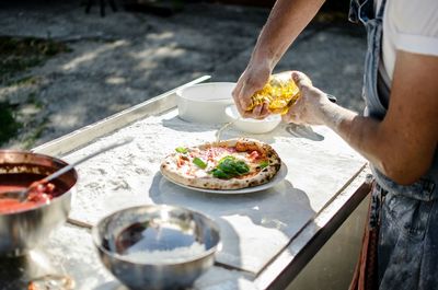 Cropped man pouring oil on pizza on plate in back yard