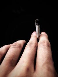 Close-up of hand holding cigarette against black background
