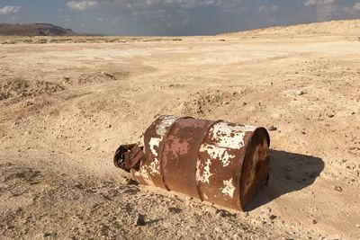Abandoned bottle on sand at beach against sky