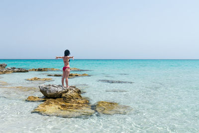 Rear view of man on rock in sea against clear sky