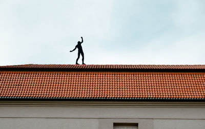 Low angle view of silhouette man on house roof against sky