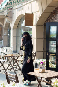 A muslim woman in national dress walks past empty tables cafe.